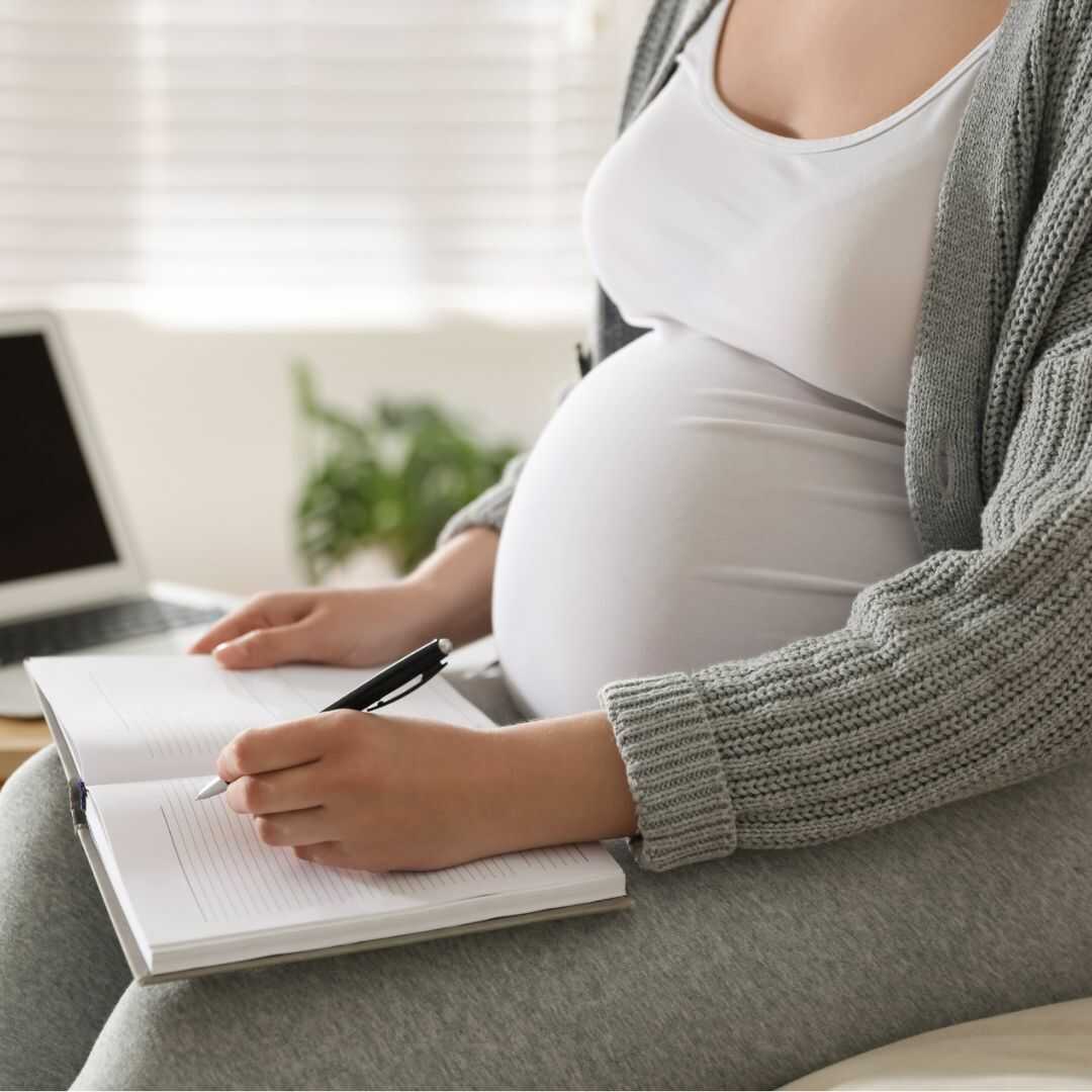Těhotná žena si něco zapisuje do deníku.