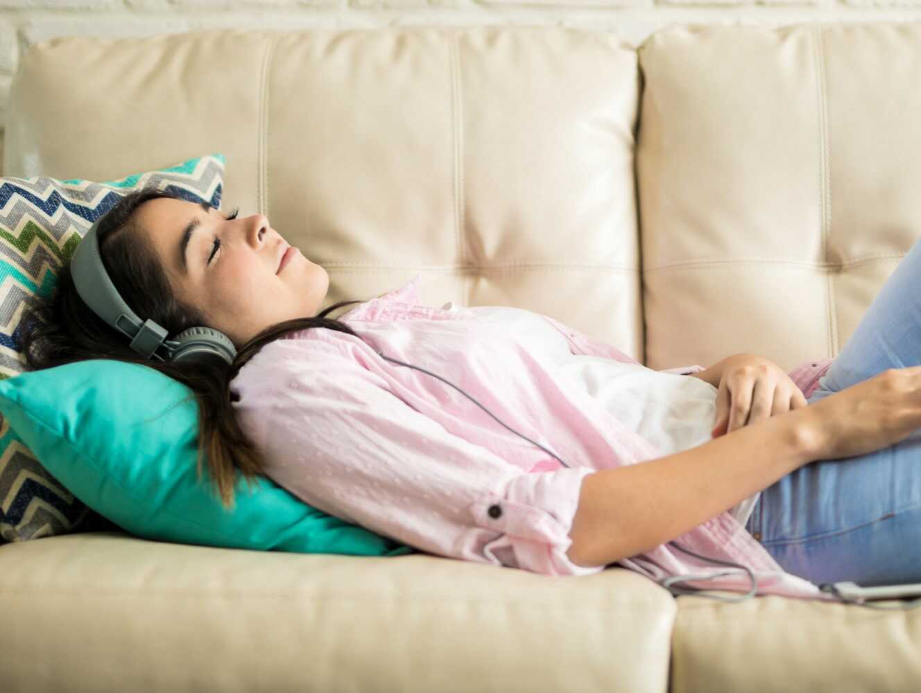 Žena ležící na gauči se sluchátky na uších.